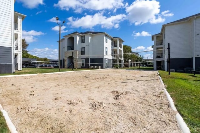 Sand volleyball court with apartment buildings exterior at Crossing Place in College Station Student Accommodation