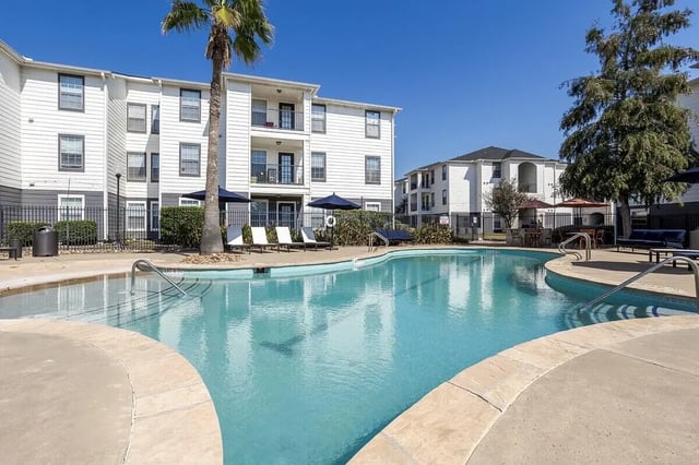 Pool area with lounge chairs and apartment buildings exterior at Crossing Place in College Station Student Accommodation