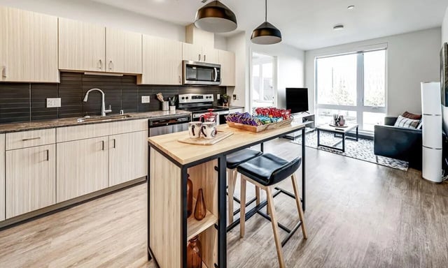 Kitchen island with stools and open plan living area at Theory U District in Seattle Student Accommodation