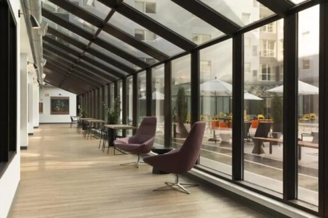 Glass enclosed hallway with chairs and tables courtyard exterior at The Quad On Delaware in Minneapolis Student Accommodation