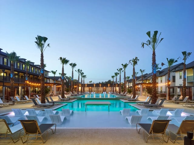 Resort style pool with lounge chairs palm trees exterior at The Junction at College Station in College Station Student Accommodation