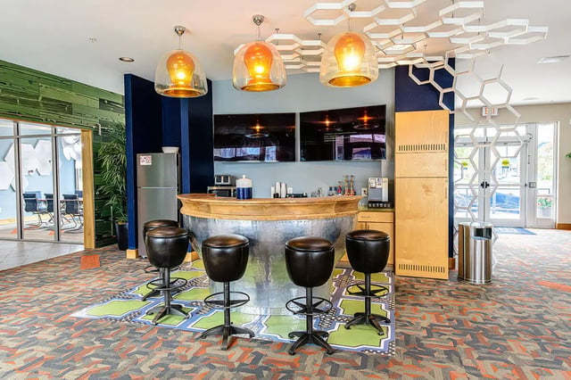 Bar with stools, TVs, refrigerator and kitchen area at The Dillon in Bloomington Student Accommodation