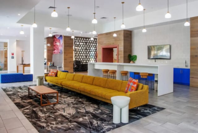 Yellow sectional sofa, coffee table, bar stools, television, living room at Apollo Tempe in Tempe Student Accommodation
