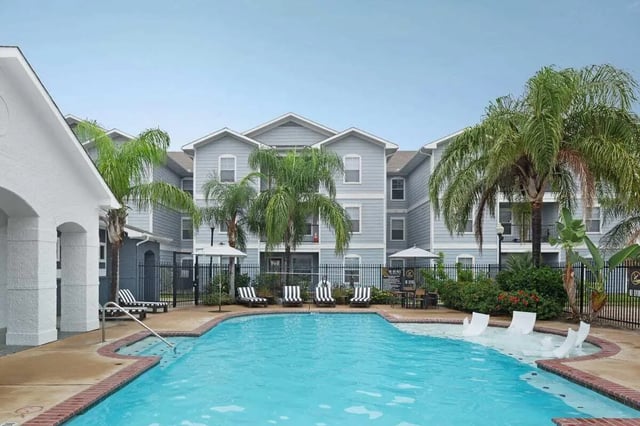 Pool with lounge chairs and palm trees exterior at The Kristi in Corpus Christi Student Accommodation