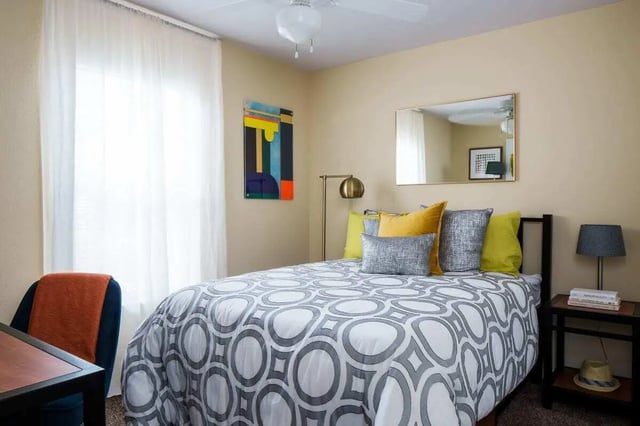 Bed with patterned duvet yellow pillows bedside table bedroom at The Kristi in Corpus Christi Student Accommodation
