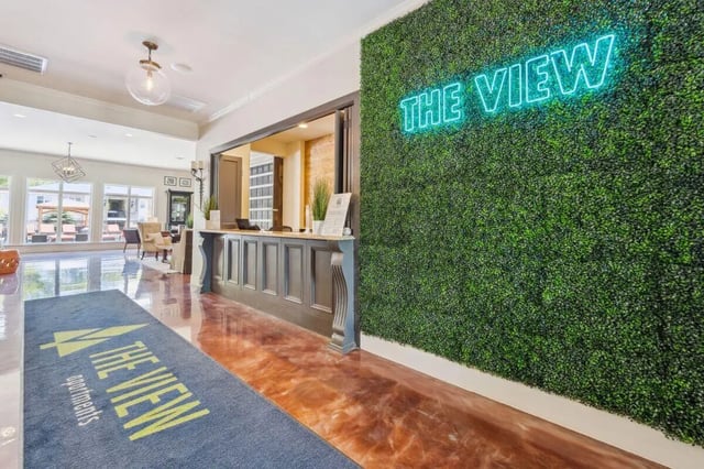 Reception desk with green wall and neon sign reception area at The View Apartments in State College Student Accommodation