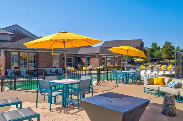 Tables chairs umbrellas lounge chairs poolside exterior at The Rendezvous Apartments in Edmond Student Accommodation