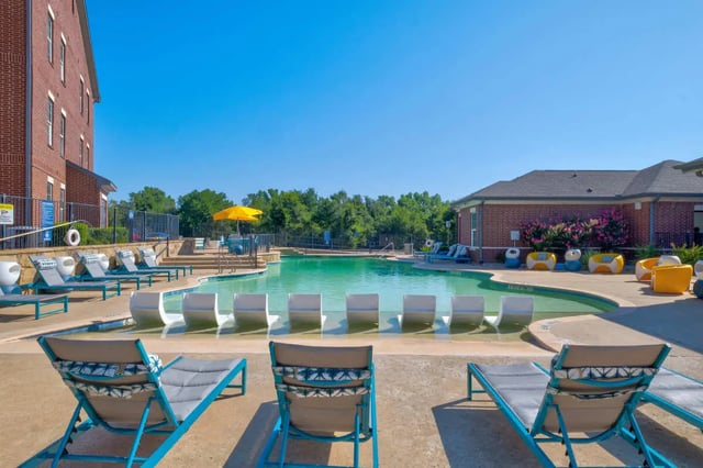 Loungers pool chairs yellow umbrella pool exterior at The Rendezvous Apartments in Edmond Student Accommodation