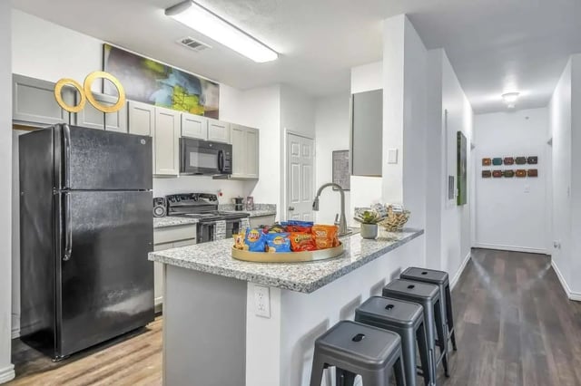 Kitchen with black refrigerator snacks and stools kitchen at The Rendezvous Apartments in Edmond Student Accommodation