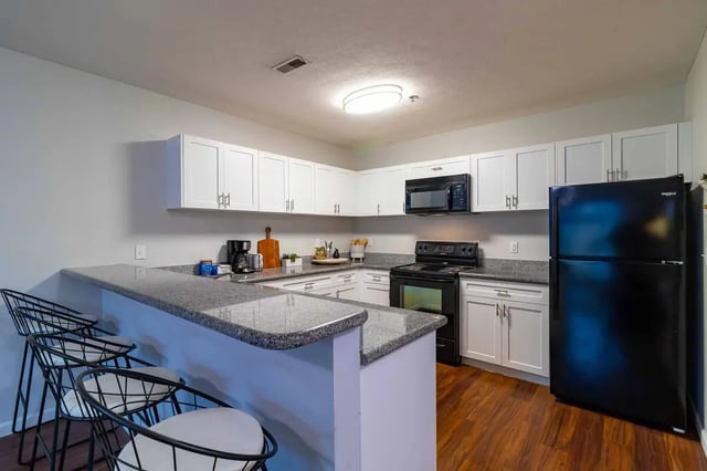 White cabinets black appliances granite counters three bar stools kitchen at PPG East Village in Columbus Student Accommodation