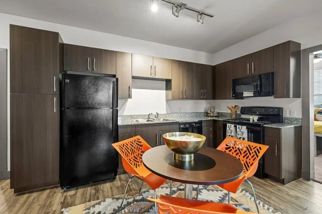 Black refrigerator dark cabinets dining table orange chairs kitchen at Holleman Crossing in College Station Student Accommodation