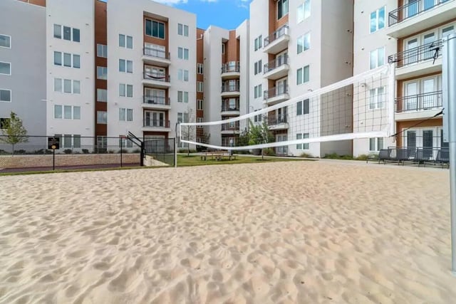 Sandy volleyball court with apartment buildings exterior at The View on the Square in San Marcos Student Accommodation