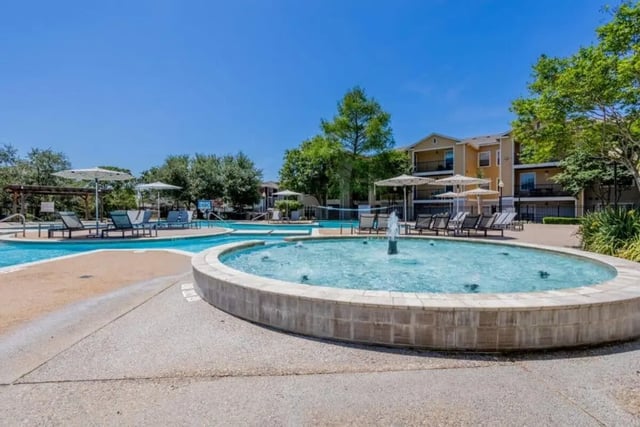 Pool with fountain lounge chairs and umbrellas exterior at University Trails College Station in College Station Student Accommodation