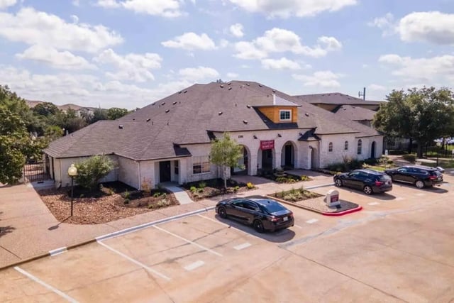 White building with cars in parking lot exterior at University Trails College Station in College Station Student Accommodation