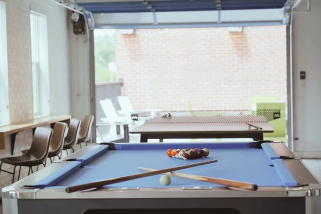 Pool table with balls cues and chairs common area at Muse on Main in Pullman Student Accommodation
