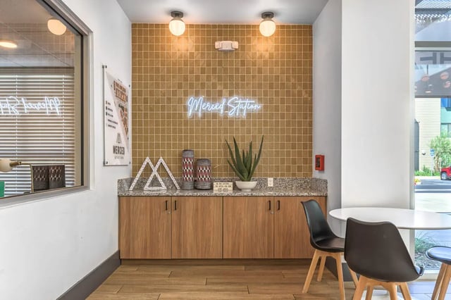 Wood cabinets plant neon sign and tables common area at Merced Station in Merced Student Accommodation