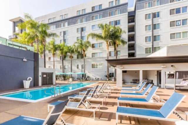 Pool lounge chairs building and palm trees exterior at University Village Towers in Riverside Student Accommodation