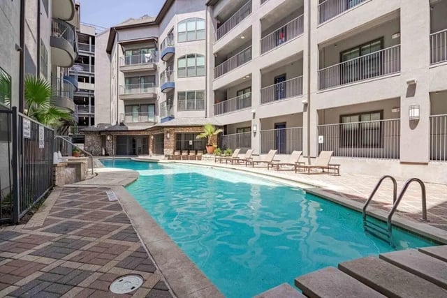 Pool with lounge chairs and apartment building exterior at Villas On Guadalupe in Austin Student Accommodation