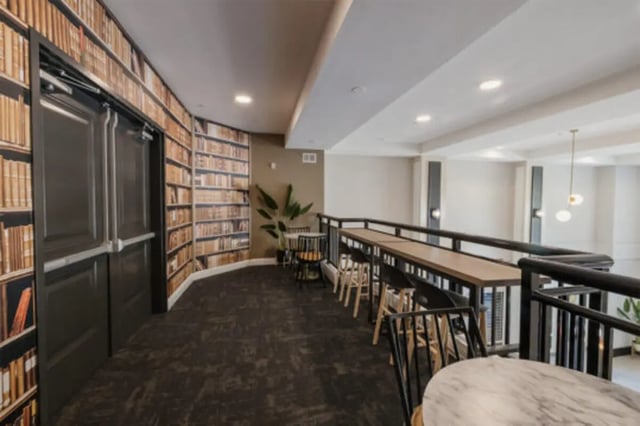 Bookshelf wallpaper double doors tables and chairs common area at The Pavilion at North Grounds Apartments in Charlottesville Student Accommodation