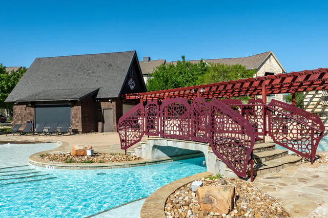 Pool with decorative bridge and lounge chairs exterior at The Cottages of College Station in College Station Student Accommodation