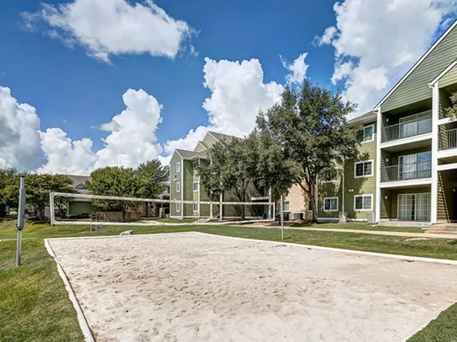 Sand volleyball court with apartment buildings exterior at Aggie Station in Bryan Student Accommodation
