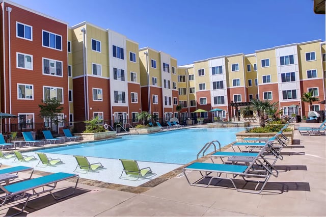 Pool with lounge chairs and apartment building exterior at The View on 10th in Waco Student Accommodation