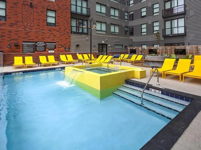 Pool with waterfall hot tub and yellow lounge chairs exterior at Campus Edge on Pierce in West Lafayette Student Accommodation