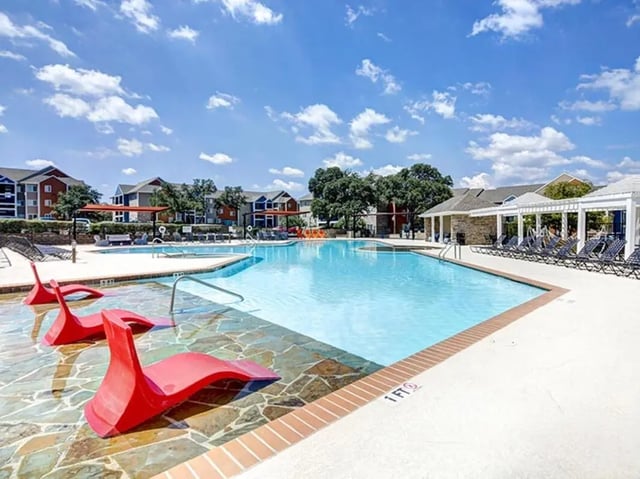 Red lounge chairs in swimming pool and apartments exterior at Campus Edge on UTSA Boulevard in San Antonio Student Accommodation