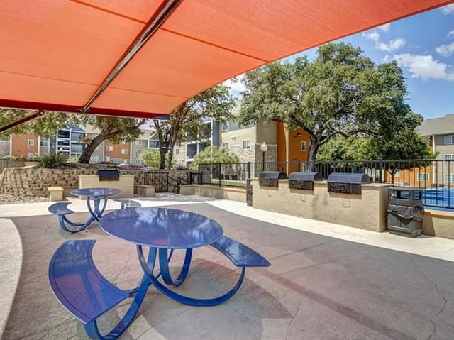 Blue picnic tables under orange awning with grills exterior at Campus Edge on UTSA Boulevard in San Antonio Student Accommodation