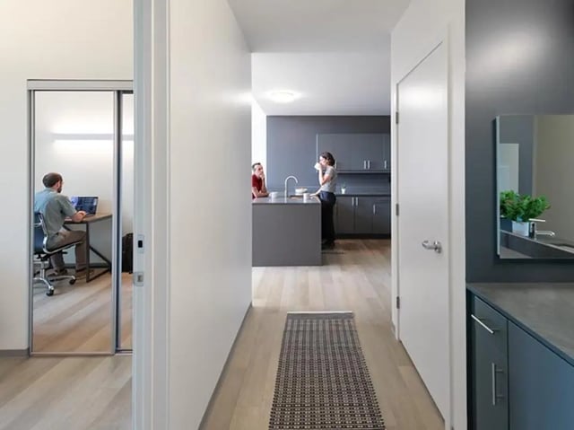 Man at desk and people in kitchen area at Graduate Junction in Cambridge Student Accommodation