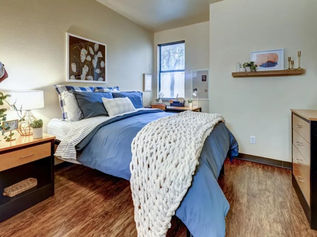 Bed with blue bedding desk lamp artwork and nightstand bedroom at The Callaway House in College Station Student Accommodation