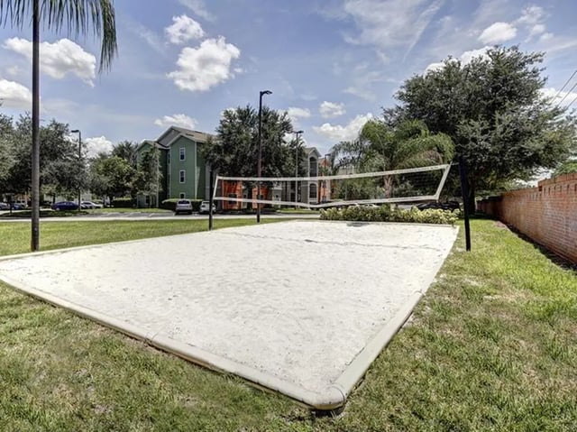 Sand volleyball court with net and apartment buildings exterior at The Village At Science Drive in Orlando Student Accommodation