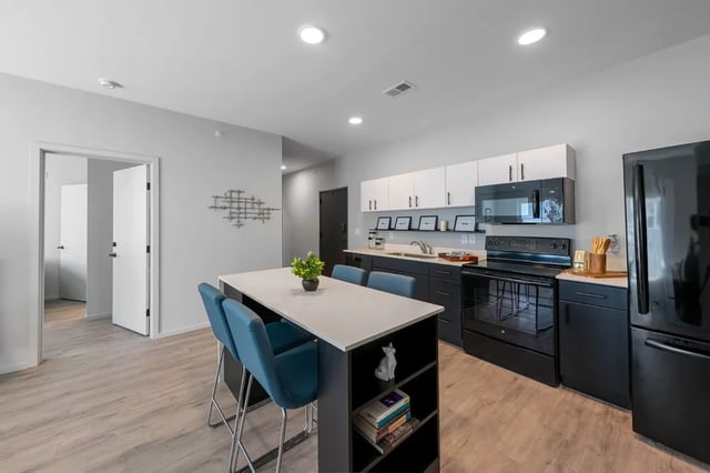 Island with chairs black appliances and white cabinets kitchen at Muse Omaha in Omaha Student Accommodation