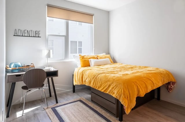 Yellow bed desk chair rug bedroom at Muse Omaha in Omaha Student Accommodation
