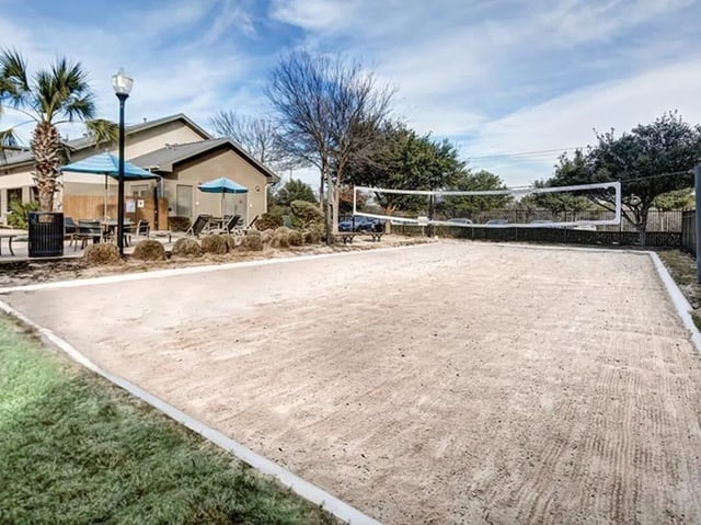 Sand volleyball court with net and building exterior at Villas at Babcock in San Antonio Student Accommodation