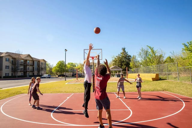Students playing basketball on an outdoor court exterior at The Flats at Norman in Norman Student Accommodation