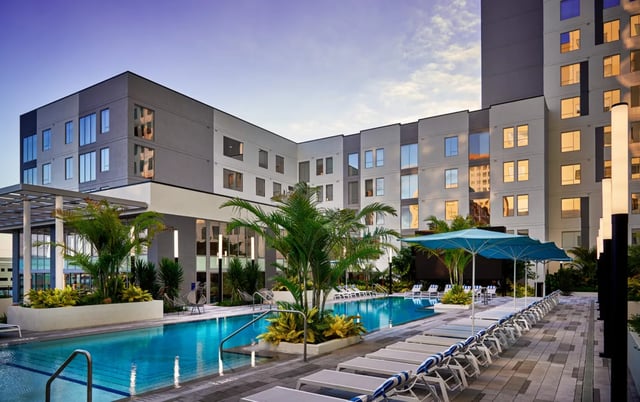 Pool lounge chairs palm trees modern building exterior at Lapis in Miami Student Accommodation