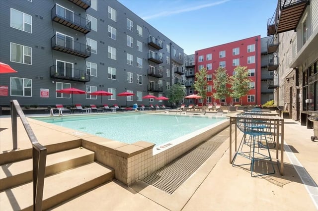 Pool with lounge chairs umbrellas and seating area exterior at The Cardinal at West Center in Fayetteville Student Accommodation