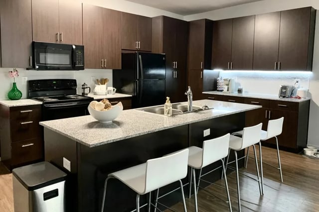 Modern kitchen island with white stools and dark cabinets kitchen at The Cardinal at West Center in Fayetteville Student Accommodation