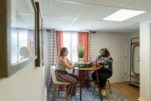 Two women at table with plants and drinks Living room at The Den Cedar Ridge in Willington Student Accommodation
