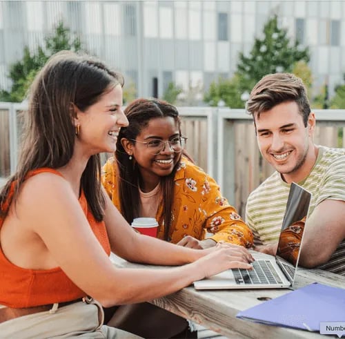 Students collaborate on laptop at outdoor table study area at Campus Walk Apartments in Buffalo Student Accommodation
