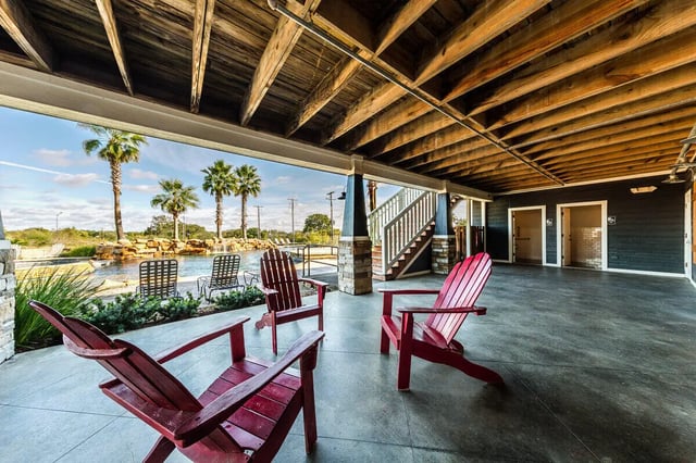 Red chairs by pool with palm trees exterior at The Reserve at College Station in College Station Student Accommodation