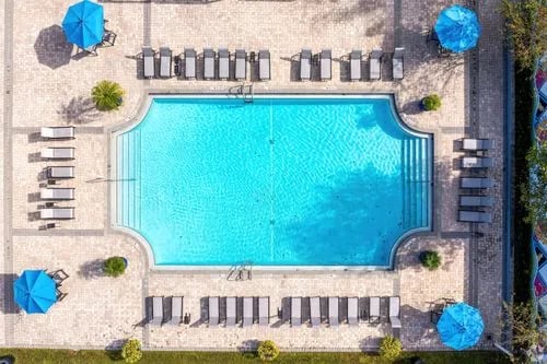Pool with lounge chairs and blue umbrellas outdoor area at Arden Villas in Orlando Student Accommodation