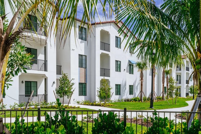 White building with balconies and palm trees exterior at The Residences at University Village in Fort Myers Student Accommodation