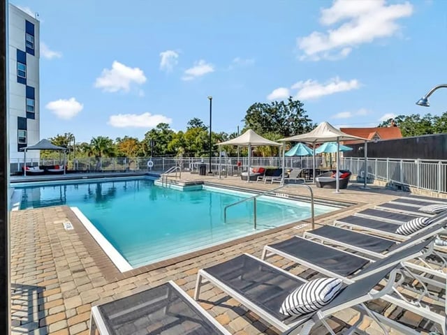 Pool with lounge chairs and umbrellas exterior at The Rowe Apartments in Tallahassee Student Accommodation