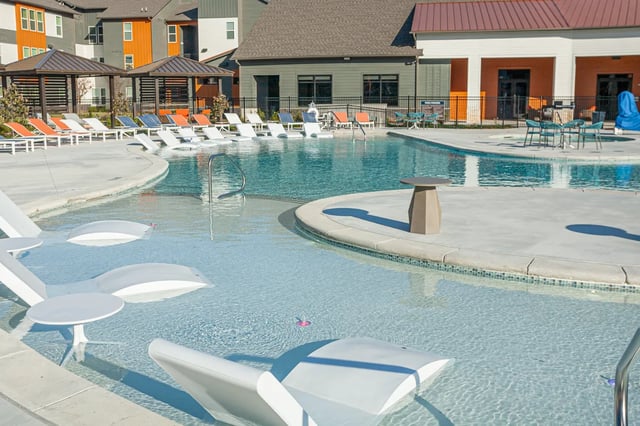 Poolside lounge chairs and tables near building exterior at Aspen Heights Fayetteville in Fayetteville Student Accommodation