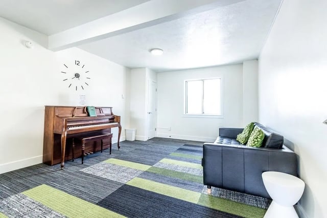 Piano couch clock patterned carpet common area at Birch Plaza and Birchwood Apartments in Rexburg Student Accommodation