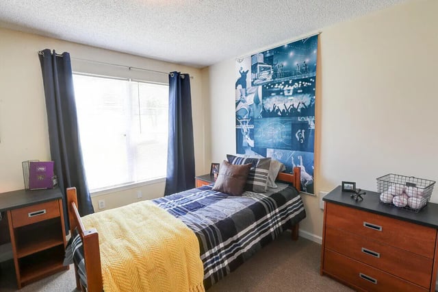 Bed with yellow blanket basketball poster dresser bedroom at Eagles Landing Apartments in Cookeville Student Accommodation