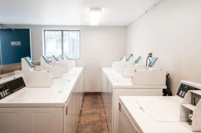 Rows of white washing machines with blue displays laundry room at Centennial Apartments in Provo Student Accommodation