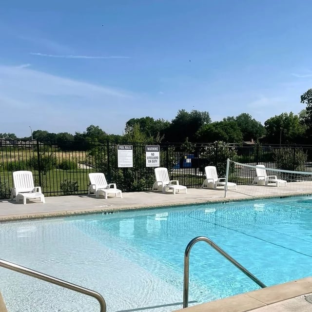 White lounge chairs surrounding a swimming pool exterior at Fireside District Apartments in Stephenville Student Accommodation